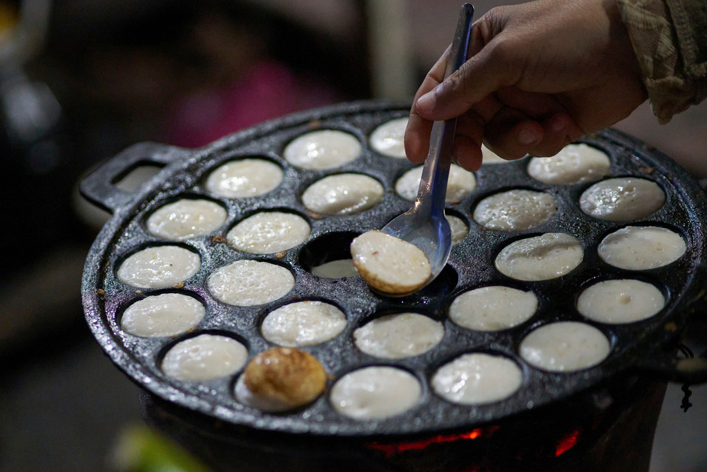 A vendor flips coconut-milk cakes known locally as khanom krok, a traditional sweet popular with both tourists and local residents, on a cast-iron pan at a morning market in Luang Prabang, Laos, Friday, Nov. 7, 2025. (AP Photo/Eugene Hoshiko)