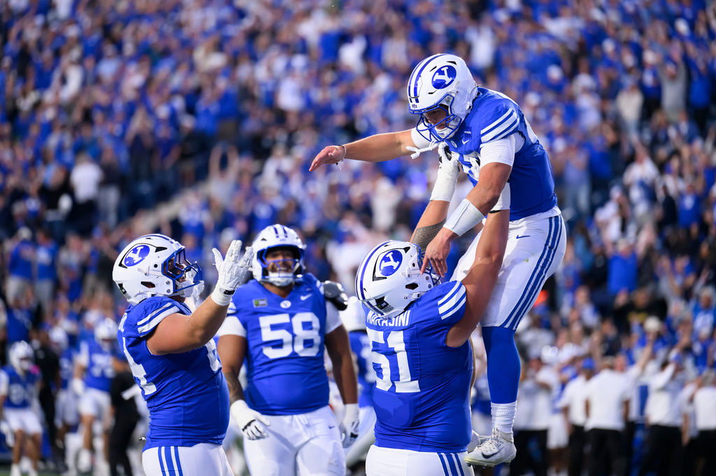 BYU offensive lineman Sonny Makasini, center right, lifts quarterback Bear Bachmeier, top, after Bachmeier ran for a touchdown during the first half of an NCAA college football game against Notre Dame, Saturday, Oct. 17, 2026, in Provo, Utah. (AP Photo/Tyler Tate)