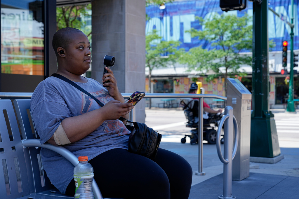 FILE - Simone Mosley waits for their ride in shade at a bus stop during an extreme heat warning July 13, 2026, in Minneapolis. (AP Photo/Ellen Schmidt, File)