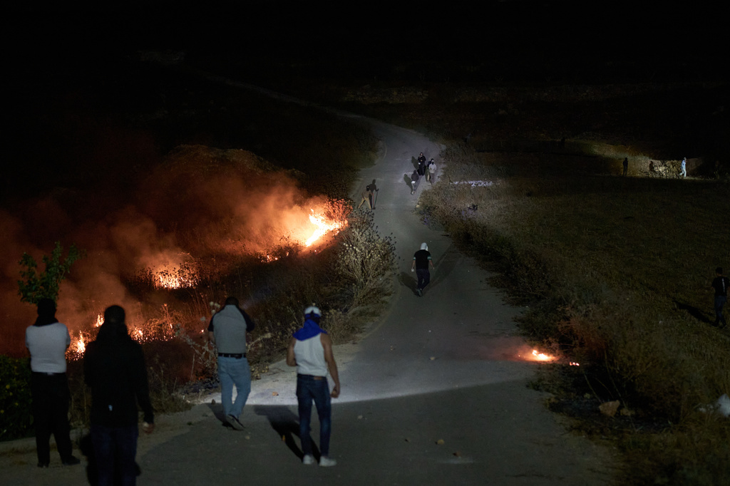 Israeli settlers, top, and Palestinians clash as brush burns along a roadside after Palestinians set it ablaze to prevent the settlers from approaching the West Bank village of Sinjil, Friday, July 17, 2026. (AP Photo/Leo Correa)