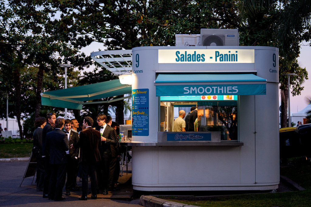 Men dressed in tuxedos enjoy drinks outside a sandwich shop before a red carpet event during the 79th international film festival, Cannes, southern France, Tuesday, May 19, 2026. (AP Photo/Andreea Alexandru)