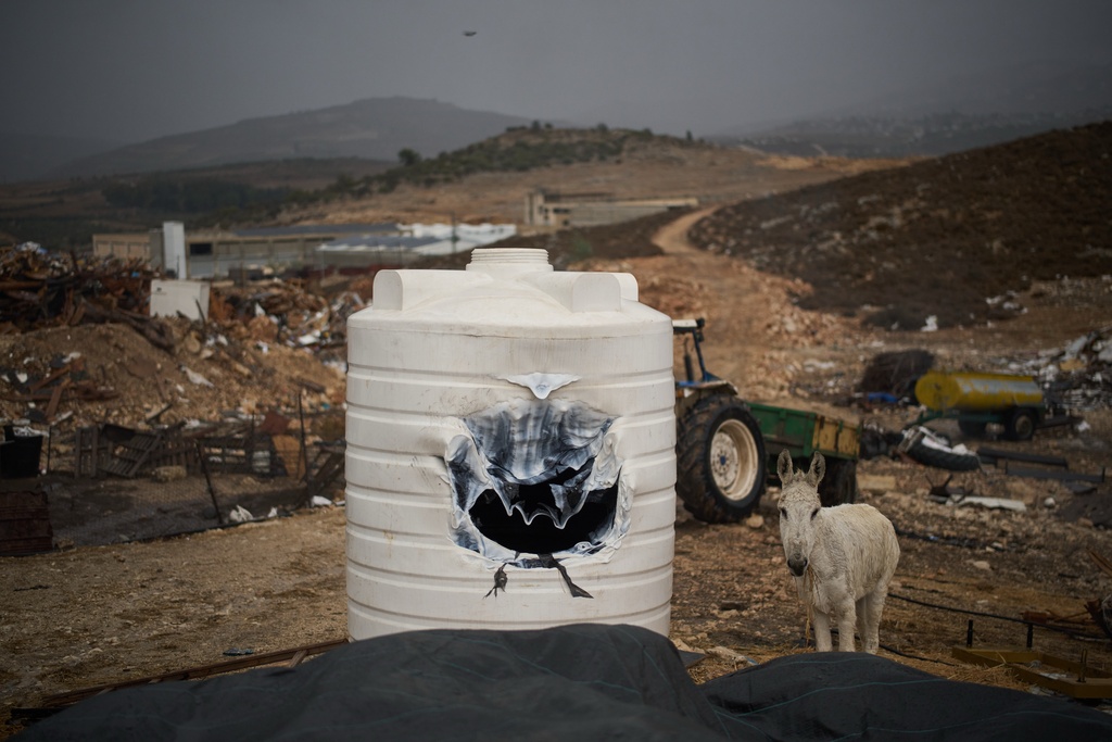 A donkey stands next to a water tank that was damaged during an attack by Israeli settlers in an industrial zone in the West Bank village of Beit Lid, near Tulkarem, Friday, Nov. 14, 2025. (AP Photo/Leo Correa)