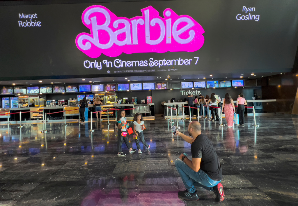 FILE - A man takes pictures of his daughters who show their tickets in front of a display panel showing the movie "Barbie" as other movie-goers, left, line up to buy tickets at a cinema, in Beirut, Lebanon, Thursday, Sept. 7, 2023. (AP Photo/Hussein Malla, File)