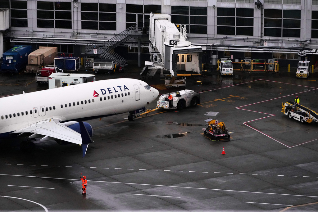 A ground crew worker signals a plane next to a Delta Airlines aircraft at Seattle-Tacoma International Airport, Thursday, Nov. 6, 2025, in SeaTac, Wash. (AP Photo/Lindsey Wasson)