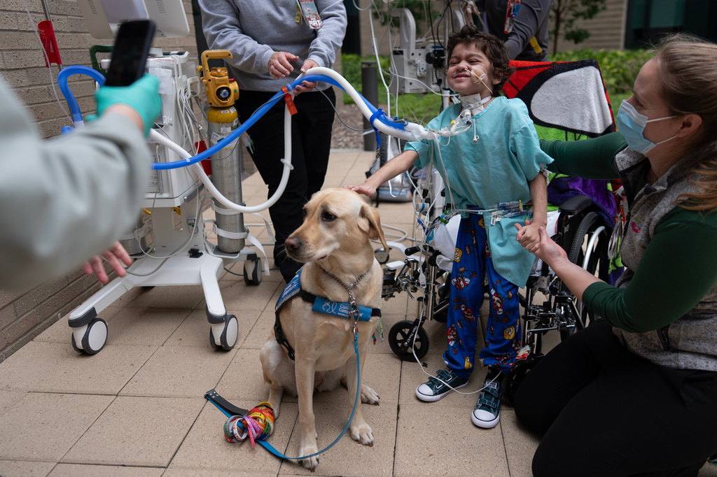 Five-year-old patient Calvin Owens stands for a photograph with Cincinnati Children's Hospital facility dog Hadley with help from physical therapist Paige Torbet, right, during a physical therapy visit on the patio of Cincinnati Children's Hospital in Cincinnati, Monday, May 4, 2026. (AP Photo/Carolyn Kaster)