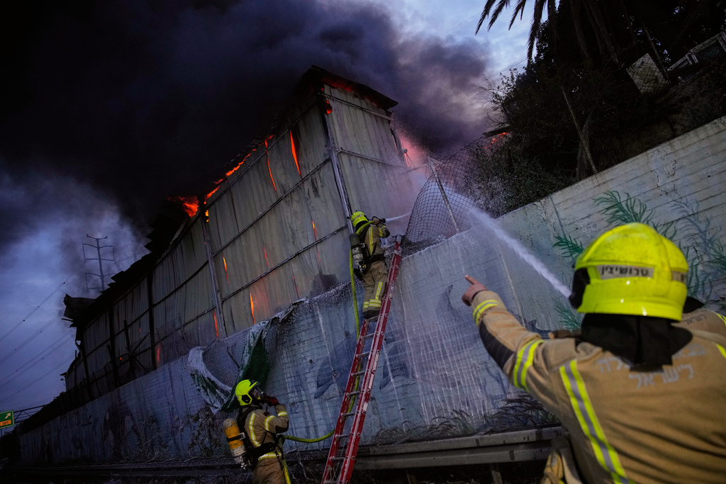 Firefighters try to extinguish flames at the site of a direct hit by an Iranian missile strike in Holon, central Israel, Friday, March 13, 2026. (AP Photo/Ohad Zwigenberg)