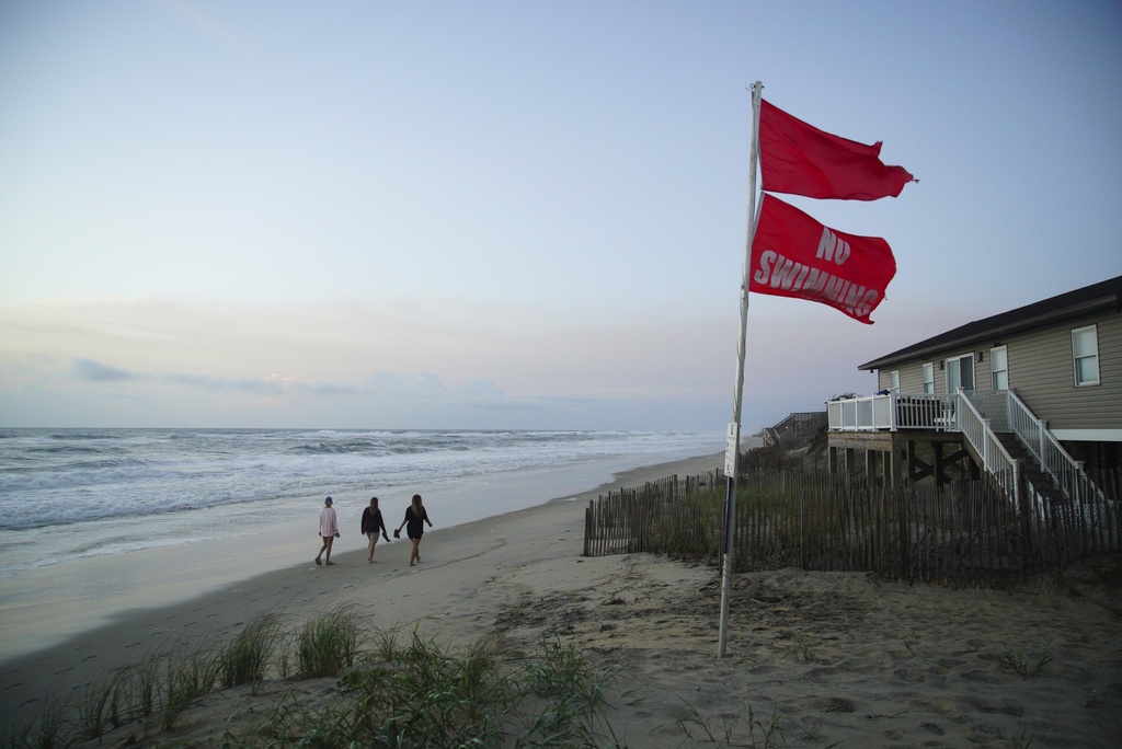 Three women walk the beach at sunrise as waves from Hurricane Erin crash ashore in Nags Head, N.C., on Wednesday, Aug. 20, 2025. (AP Photo/Allen G. Breed)