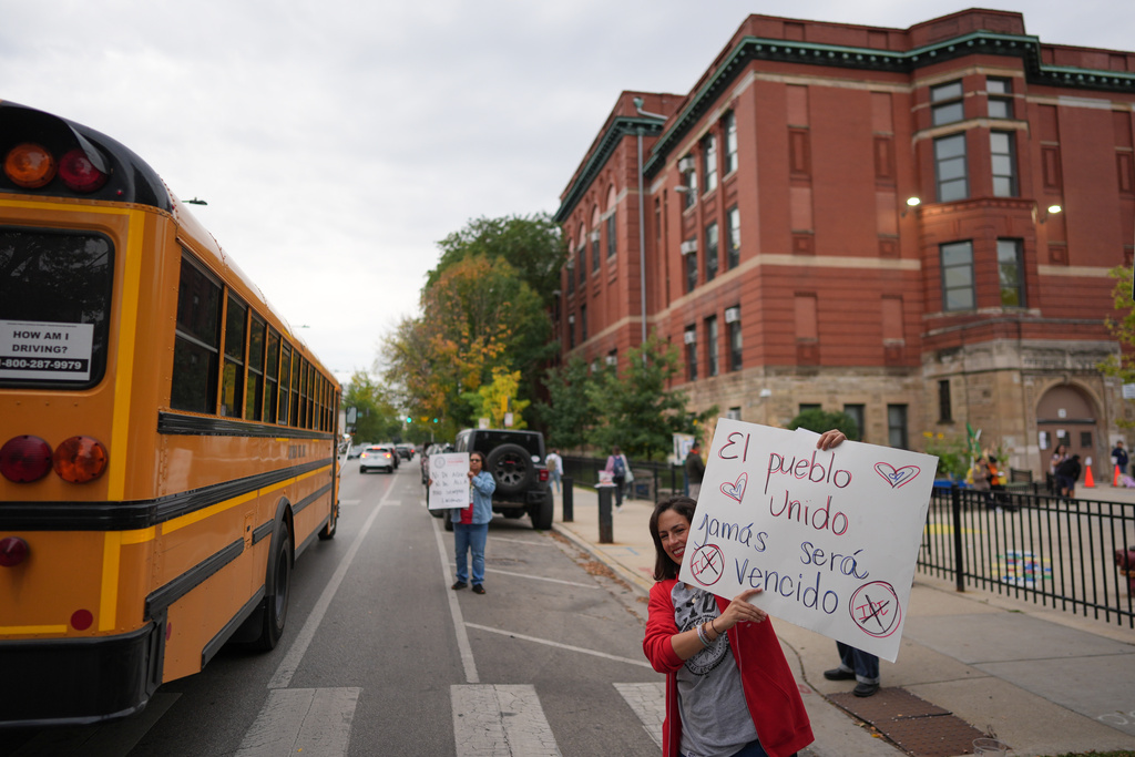 First grade teacher Maria Heavener holds a sign that reads in Spanish, "The people, united, will never be defeated," as she participates in Sidewalk Solidarity, a weekly show of support by Chicago Teachers Union members for the school's immigrant community in Chicago's Logan Square neighborhood, Friday, Oct. 17, 2025. (AP Photo/Rebecca Blackwell)