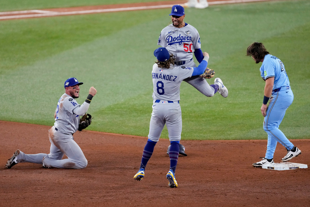 Los Angeles Dodgers' Mookie Betts (50) leaps into the arms of Kiké Hernández (8) as Miguel Rojas, left, pumps his fist after Toronto Blue Jays' Addison Barger, right, was forced out to end Game 6 of baseball's World Series, Friday, Oct. 31, 2025, in Toronto. (AP Photo/Ashley Landis)