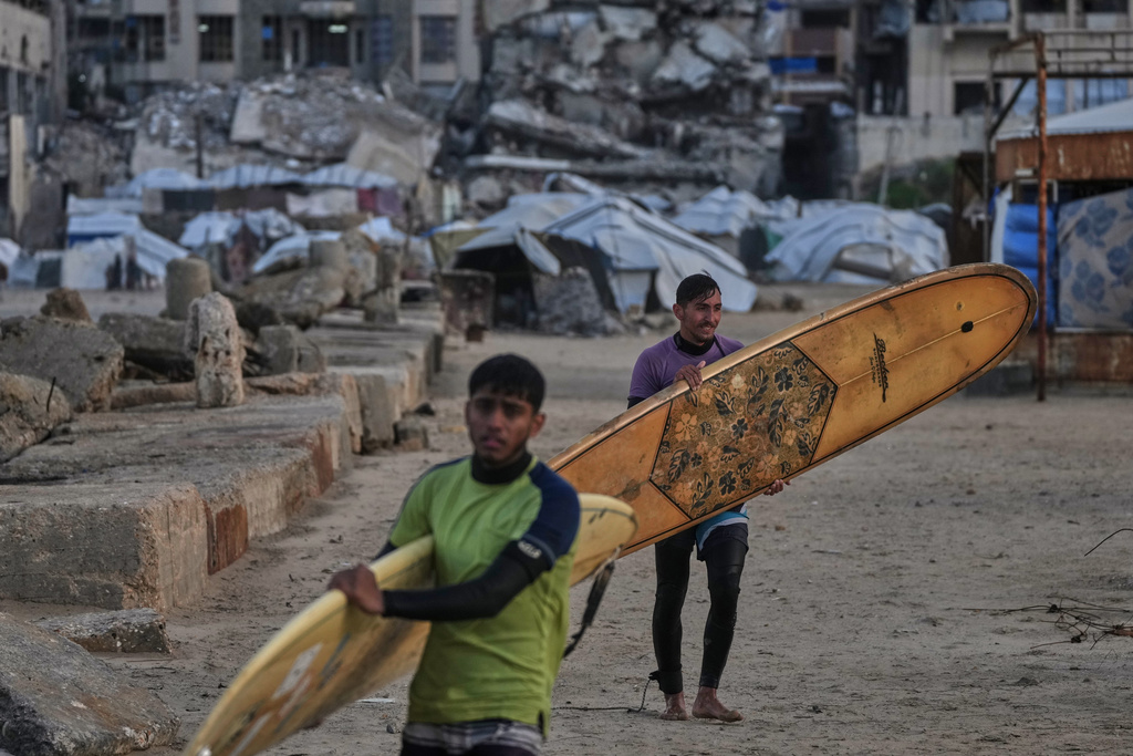 Palestinian Khalil Abu Jayyab, front, and Tahseen Abu Assi carry their surfing boards as they enter the water along a damaged shoreline in Gaza City, Sunday, Dec. 28, 2025. (AP Photo/Jehad Alshrafi)