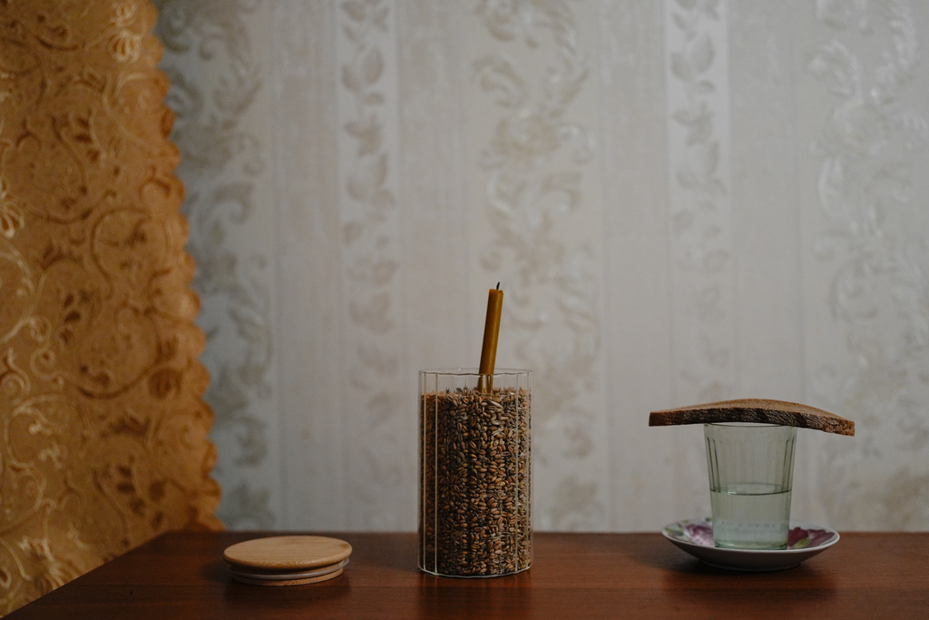 Bread rests on a glass of water and a candle sits in a jar of grain in the Savchenko family apartment as part of a Ukrainian mourning tradition, three weeks after the death of Anatoliy, Friday, Oct. 31, 2025, in Chernihiv, Ukraine. (AP Photo/Julia Demaree Nikhinson)