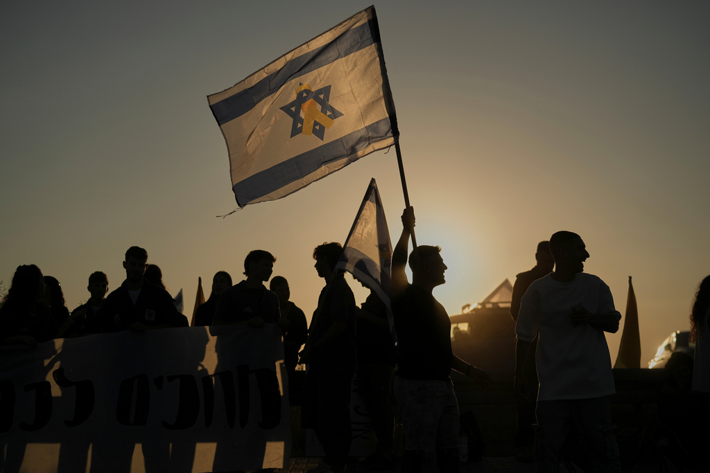 People hold Israeli flags as they gather before the release of Israeli hostages held in Gaza, outside a military base near Reim, southern Israel, on Monday, Oct. 13, 2025. (AP Photo/Leo Correa)