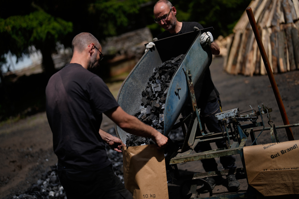 Brothers Immo and Sascha Feldmer put charcoal into paper bags after weighing it at their traditional production site near Hasselfelde in Germany's Harz, Germany, Thursday, June 18, 2026. (AP Photo/Matthias Schrader)