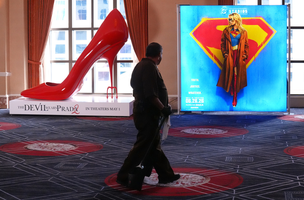A maintenance worker walks past advertisements for the upcoming films "The Devil Wears Prada," left, and "Supergirl" during the opening day of CinemaCon 2026, the official convention of Cinema United, on Monday, April 13, 2026, at Caesars Palace in Las Vegas. (AP Photo/Chris Pizzello)