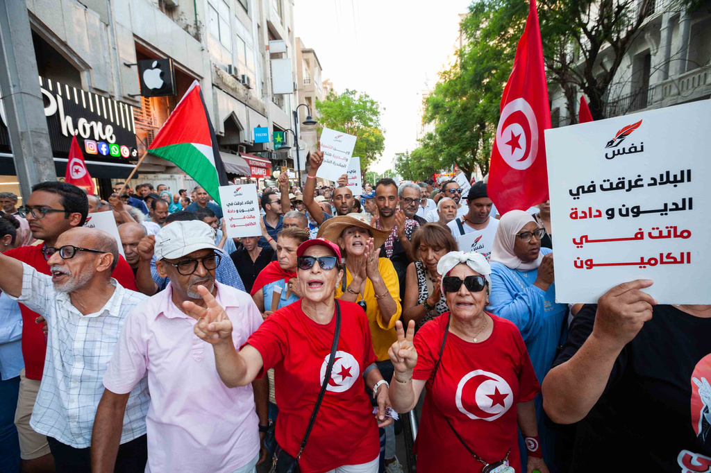 People take part in a protest against rising prices, declining purchasing power and shortages of basic goods in Tunis, Tunisia, Thursday, Aug. 20, 2026. Banner in Arabic reads "The country is drowning in debt". (AP Photo/Ons Abid)