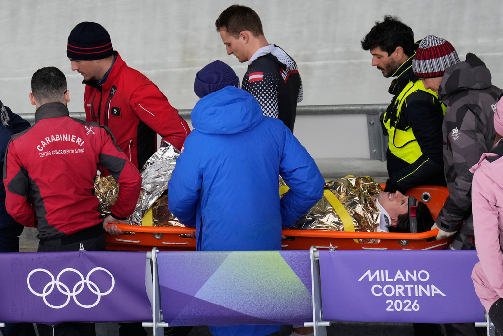 Team members and rescue workers carry an injured athlete after Austria's team Jakob Mandlbauer, Daniel Bertschler, Sebastian Mitterer and Daiyehan Nichols-Bardi crashed during a four man bobsled run at the 2026 Winter Olympics, in Cortina d'Ampezzo, Italy, Saturday, Feb. 21, 2026. (AP Photo/Aijaz Rahi)