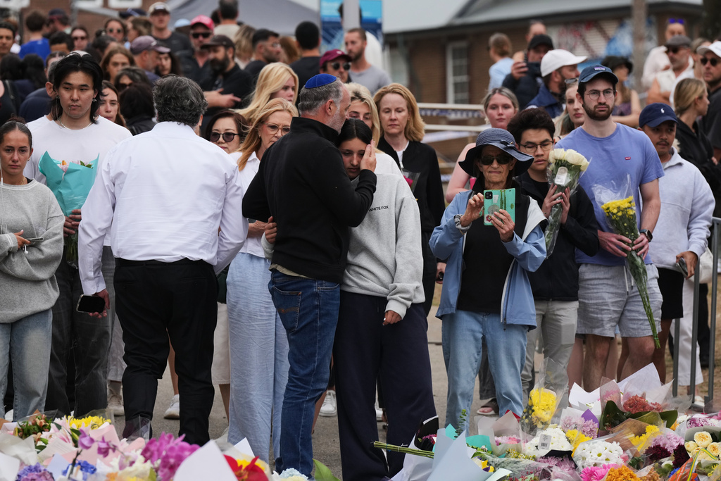 People offer flowers and hugs at a floral memorial during a tribute for victims of Sunday's shooting at the Bondi Pavilion at Bondi Beach on Tuesday, Dec. 16, 2025, in Sydney, Australia. (AP Photo/Mark Baker)
