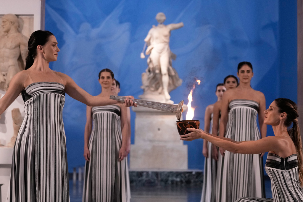 High Priestess Mary Mina, left, lights a torch from the Olympic flame during the flame lighting ceremony for the Milan Cortina 2026 Winter Olympics, at the archaeological museum of Olympia, Greece, Wednesday, Nov. 26, 2025. (AP Photo/Thanassis Stavrakis)