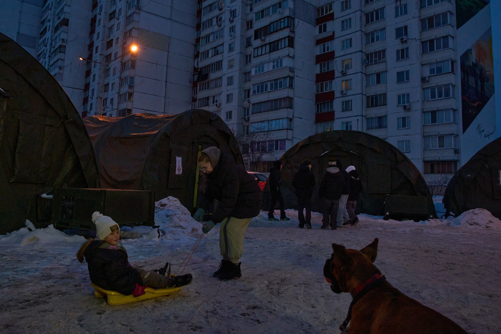 A girl on a sled plays with a dog near an emergency tent camp in a residential neighborhood as repeated Russian air attacks on the country's energy sector leave people without power, heating and water in the harshest winter in decades in Kyiv, Ukraine, Sunday, Feb. 8, 2026. (AP Photo/Efrem Lukatsky)