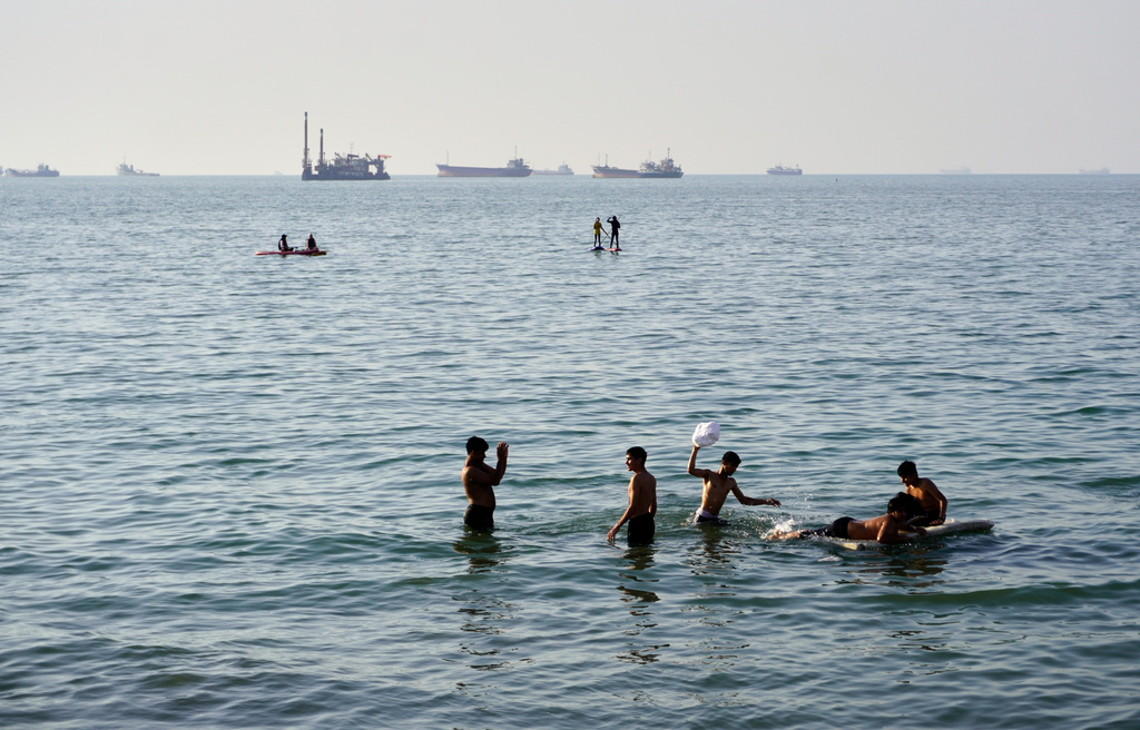 Residents swim and play in the waters of the Strait of Hormuz while cargo ships and commercial vessels lie anchored in the distance off Bandar Abbas, Iran, Wednesday, June 10, 2026.(Razieh Poudat/ISNA via AP)