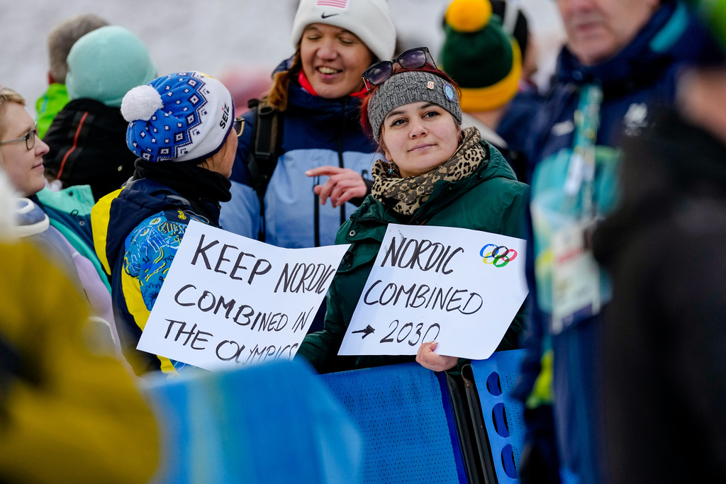 Fans hold sigs while watching the ski jumping of the nordic combined individual Gundersen large hill/10km at the 2026 Winter Olympics, in Predazzo, Italy, Tuesday, Feb. 17, 2026. (AP Photo/Matthias Schrader)