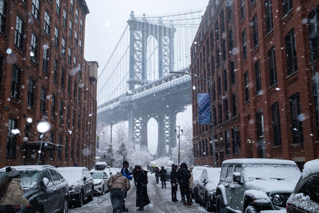 People gather on Washington Street in front of Manhattan Bridge during a snowfall, Sunday, Dec. 14, 2025, in the Brooklyn Borough of New York. (AP Photo/Adam Gray)