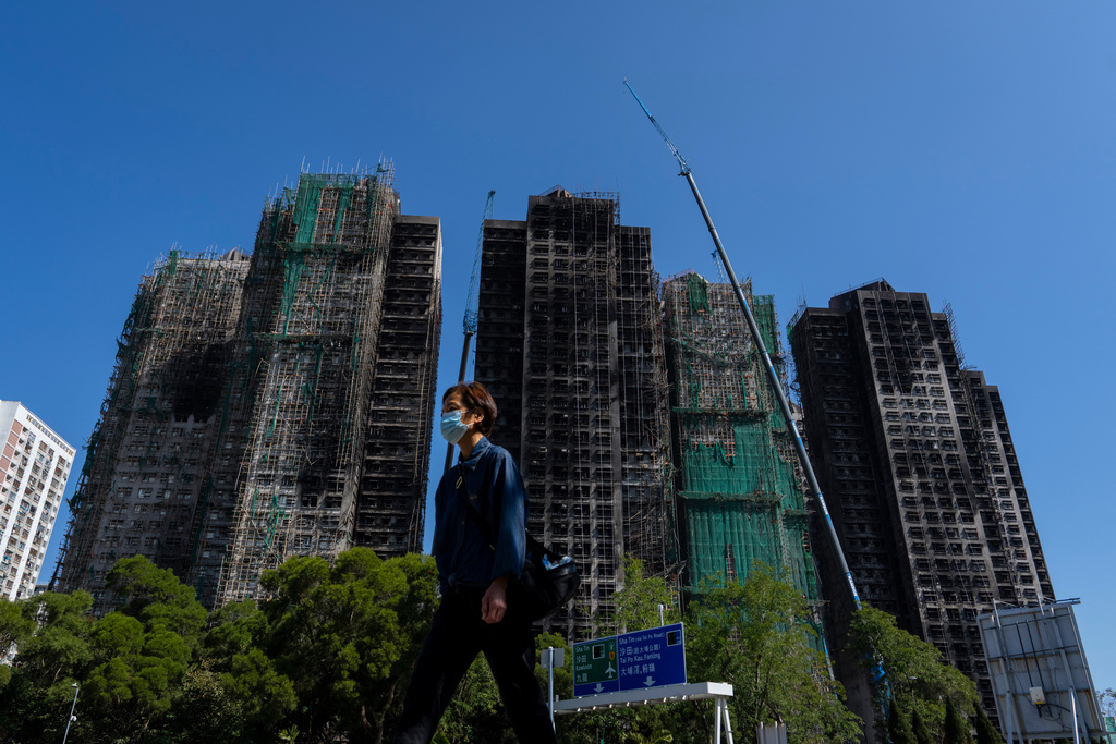 A pedestrian walks past the fire-ravaged residential towers of the Wang Fuk Court apartment complex, in the Tai Po district of Hong Kong, Friday, Feb. 6, 2026. (AP Photo/Chan Long Hei)