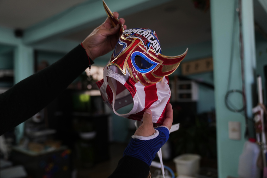 A worker holds up the a Great American wrestling mask at Alma Guadalupe Zuñiga's mask making workshop in Mexico City, Saturday, Feb. 7, 2026. (AP Photo/Marco Ugarte)