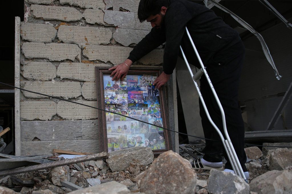 Ali Fahos, a member of Hezbollah's health unit, places portraits of colleagues killed during the previous war with Israel next to a building destroyed in an Israeli airstrike, in Jibchit, southern Lebanon, Friday, April 17, 2026, following a ceasefire between Israel and Hezbollah. (AP Photo/Hassan Ammar)