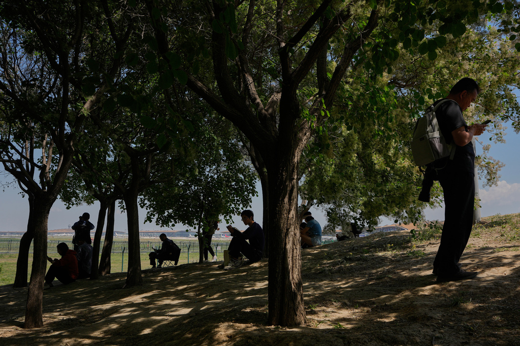 People take a rest underneath trees at a viewing platform of a public park as they wait to catch a glimpse of the arrival of U.S. Air Force Boeing C-17 Globemaster III transport aircraft to the Beijing International Capital Airport ahead of U.S. President Donald Trump's visit, in Beijing, Monday, May 11, 2026. (AP Photo/Andy Wong)