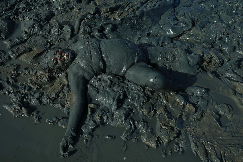 A reveler frolics in layers of mud during the Mud Block carnival party in Paraty, Brazil, Saturday, Feb. 14, 2026. (AP Photo/Andre Penner)
