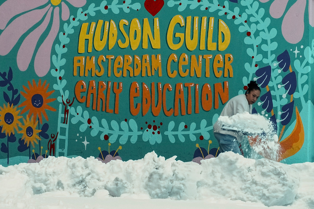 A woman clears snow from a walk outside a preschool, Tuesday, Feb. 24, 2026, in New York. (AP Photo/Eduardo Munoz Alvarez)