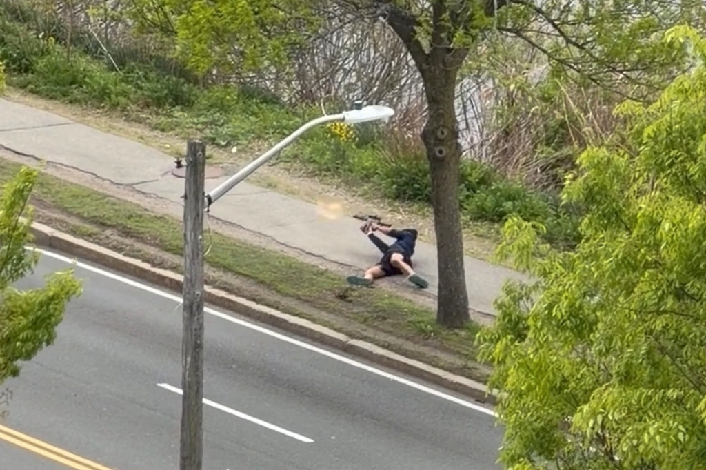This image taken from video provided by Youssef Adel, shows a man with an assault-style rifle firing his weapon at a busy road outside at in Cambridge, Mass. on Monday, May 11, 2026. (Youssef Adel via AP)