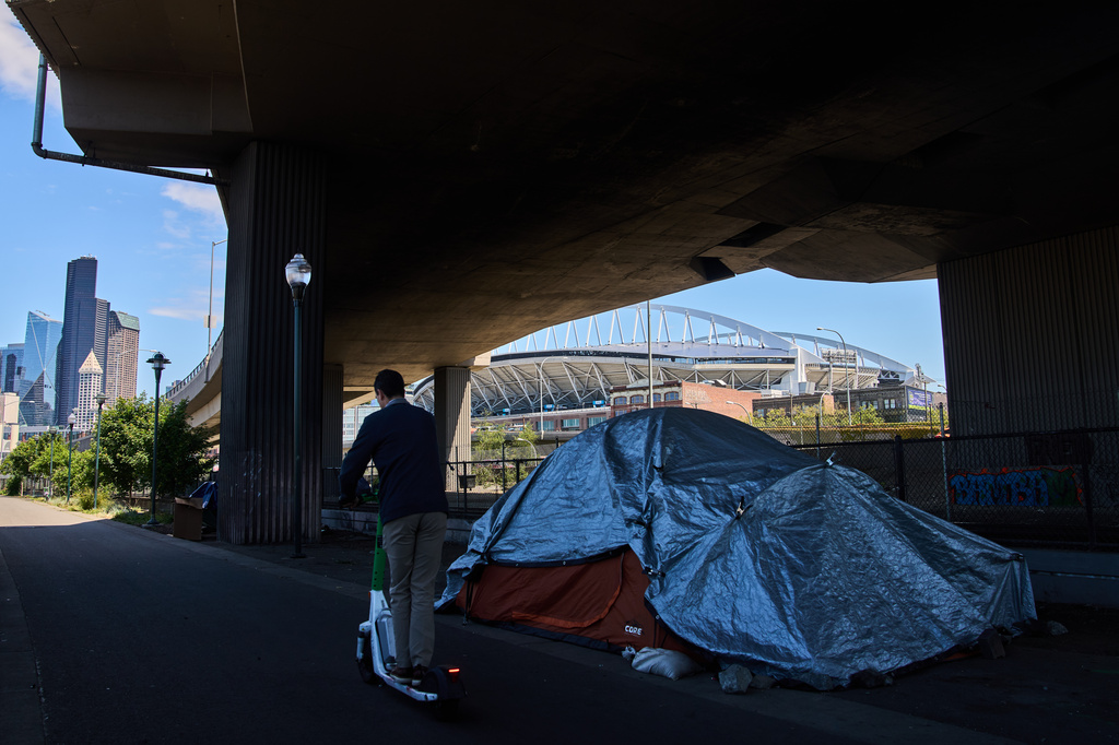 Seattle Stadium is seen in the background as a person rides a scooter past a series of tents on a trail near the stadium ahead of the 2026 FIFA World Cup soccer matches Wednesday, May 27, 2026, in downtown Seattle. (AP Photo/Lindsey Wasson)