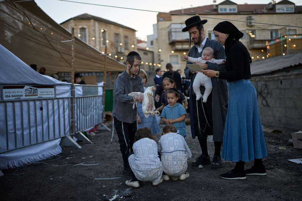 An ultra-Orthodox Jewish boy swings a chicken over a two girls heads in Jerusalem, Tuesday, Sept. 30, 2025, as part of the Kaparot ritual before the Jewish holiday of Yom Kippur. (AP Photo/Ohad Zwigenberg)