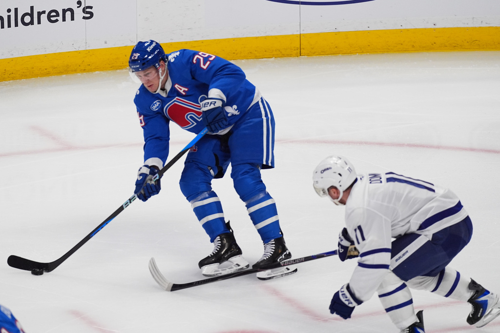 Colorado Avalanche center Nathan MacKinnon, back, passes the puck as Toronto Maple Leafs center Max Domi defends in the first period of an NHL hockey game, Monday, Jan. 12, 2026, in Denver. (AP Photo/David Zalubowski)