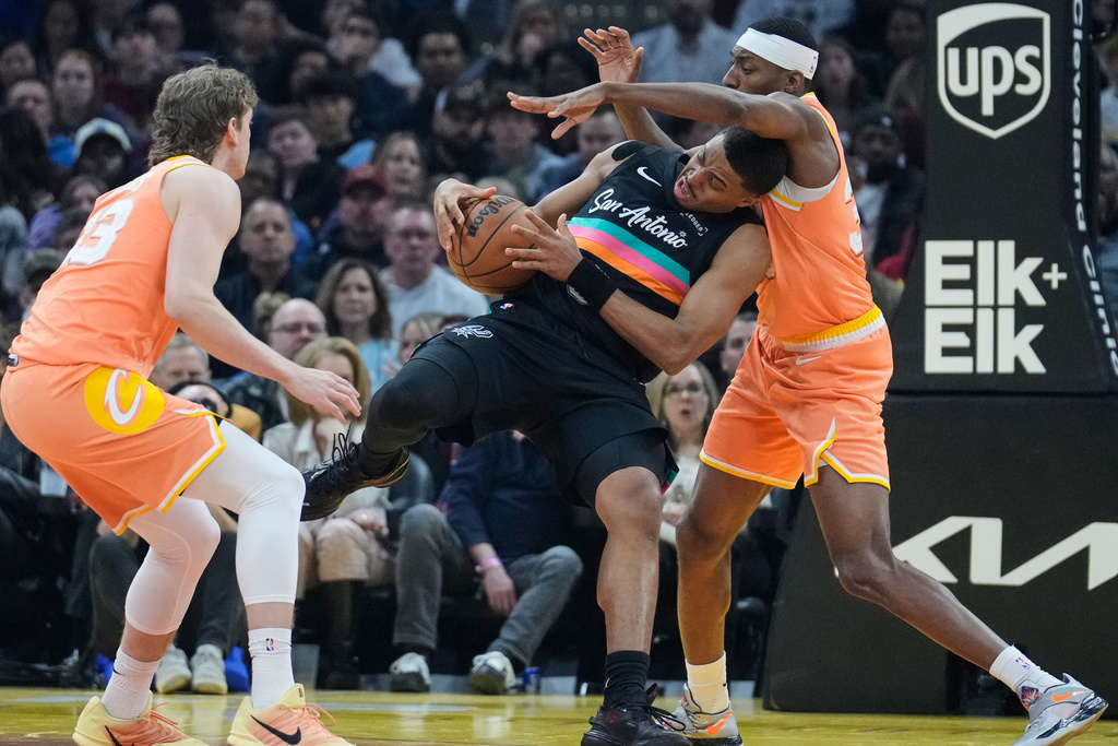San Antonio Spurs forward Keldon Johnson, center, loses control of the ball between Cleveland Cavaliers forward Luke Travers, left, and forward Nae'Qwan Tomlin, right, in the first half of an NBA basketball game Friday, Dec. 5, 2025, in Cleveland. (AP Photo/Sue Ogrocki)