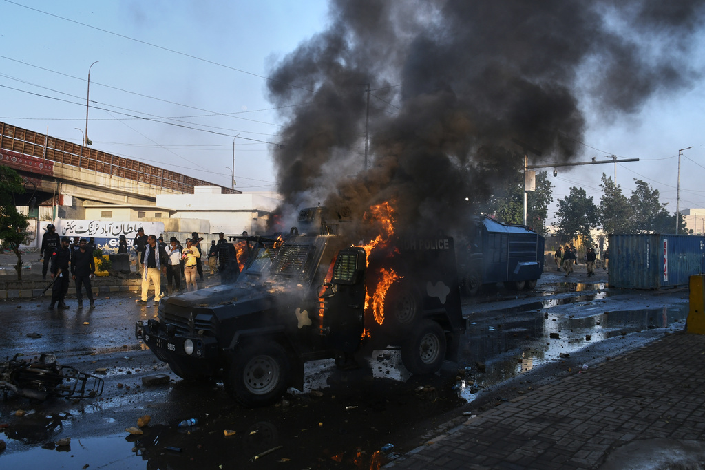 Police officers walk past a burning police's armoured vehicle, which was set on fire by Shiite Muslims during a protest to condemn the killing of Iranian Supreme Leader Ayatollah Ali Khamenei, in Karachi, Pakistan, Sunday, March 1, 2026. (AP Photo/Ali Raza)