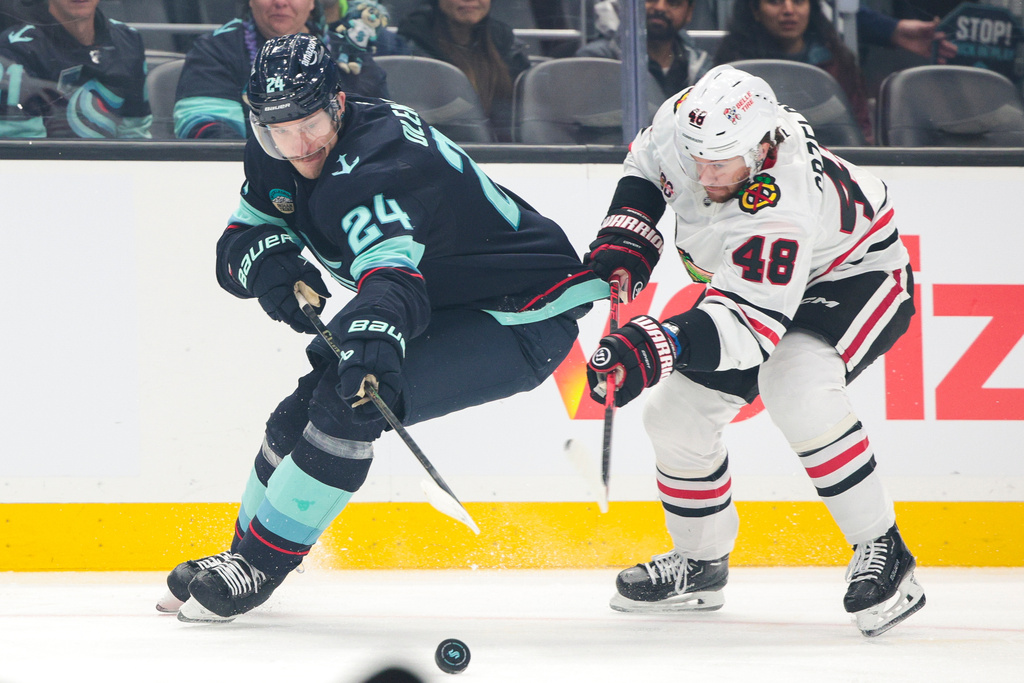 Seattle Kraken defenseman Jamie Oleksiak (24) and Chicago Blackhawks defenseman Matt Grzelcyk (48) go for the puck during the first period of an NHL hockey game Monday, Nov. 3, 2025, in Seattle. (AP Photo/Jason Redmond)