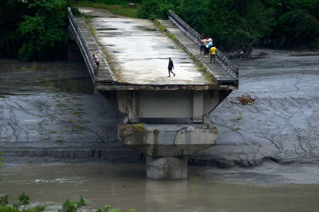 People stand on remnants of a bridge which spanned across Trishuli river and was washed away in flash floods, in Dhading District, Nepal, Sunday, Aug. 30, 2026. (AP Photo/Niranjan Shrestha)