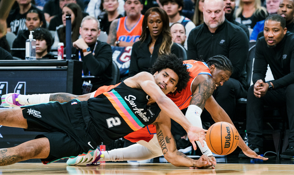 San Antonio Spurs guard Dylan Harper (2) and Oklahoma Thunder guard Jalen Williams (8) scramble for a loose ball during the first half of an NBA basketball game in San Antonio, Tuesday, Dec. 23, 2025. (AP Photo/Rodolfo Gonzalez)