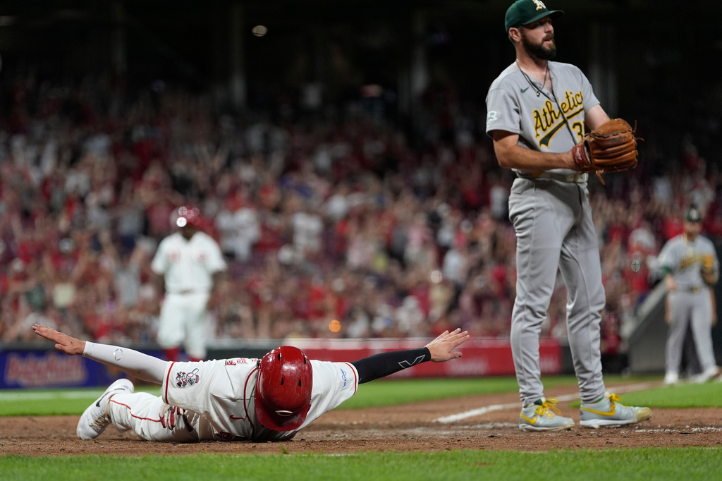 Cincinnati Reds' Sal Stewart, left, reacts after diving across home plate to score the go-ahead run on a wild pitch by Athletics pitcher Hogan Harris, right, during the eight inning of a baseball game in Cincinnati, Tuesday, Aug. 4, 2026. (AP Photo/Carolyn Kaster)
