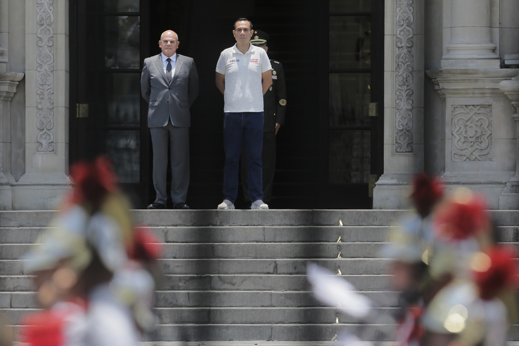 Photographed through a gate, Peru's President Jose Jeri, right, stands with Prime Minister Ernesto Alvarez during the changing of the guard ceremony at the government palace in Lima, Peru, Tuesday, Feb. 17, 2026. (AP Photo/Gerardo Marin)