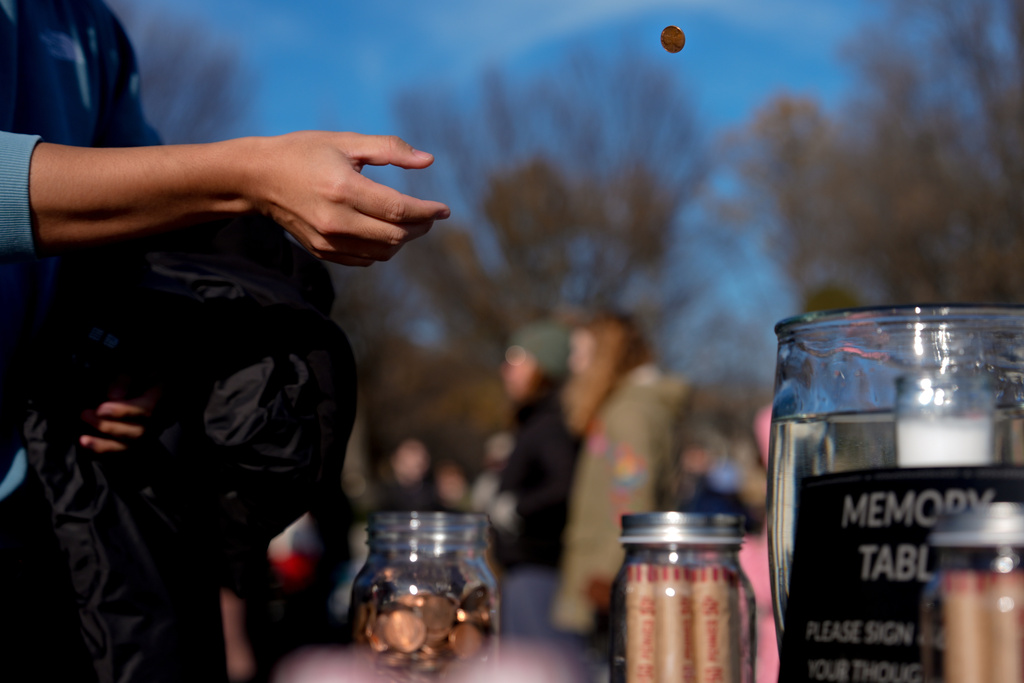 A person tosses a penny into a jar during a mock funeral for the penny, which was discontinued earlier this year, Saturday, Dec. 20, 2025, in front of the Lincoln Memorial in Washington. (AP Photo/Julia Demaree Nikhinson)