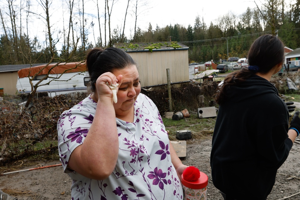 Rosenda Quintero, center, and her daughter Mariana Martinez walk towards the backyard of her home which was flooded in the Three Rivers Mobile Home Park on the Snohomish River in near Monroe on Saturday, Dec. 13, 2025. (Karen Ducey/The Seattle Times via AP)