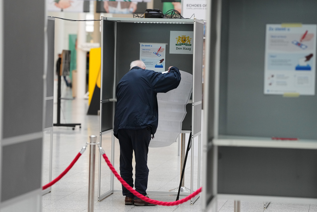 A man unfurls a sheet listing all the candidates as he stands in a voting booth at a polling station during general elections in The Hague, Netherlands, Wednesday, Oct. 29, 2025. (AP Photo/Peter Dejong)