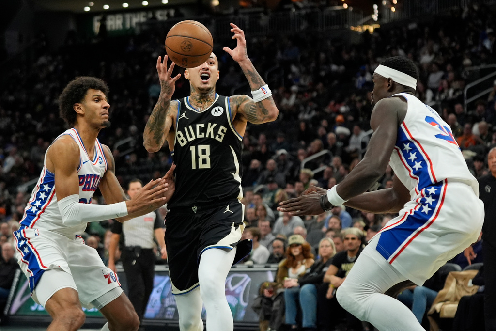Milwaukee Bucks' Kyle Kuzma (18) controls the ball as he drives to the basket between Philadelphia 76ers' Dominick Barlow, left, and Adem Bona during the first half of an NBA basketball game, Friday, Dec. 5, 2025, in Milwaukee. (AP Photo/Aaron Gash)