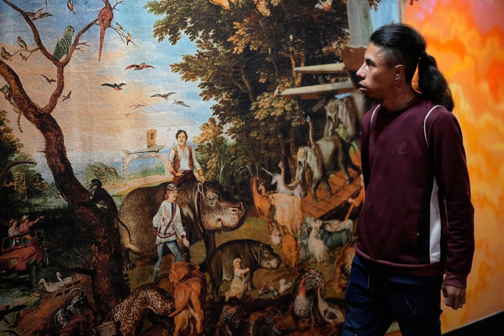 A visitor looks at a tapestry titled: "The Great Narco Ark" by Carlos Castro during an exhibit featuring Colombian artists that seeks to critique the hippos brought by late drug lord Pablo Escobar in Bogota, Colombia, Thursday, Nov. 6, 2025. (AP Photo/Fernando Vergara)