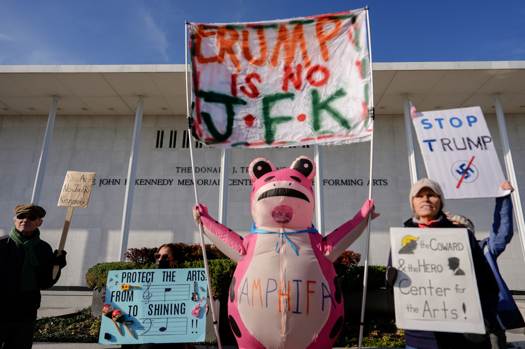 FILE - Demonstrators, including Nadine Siler, of Waldorf, Md., dressed in a pink frog costume, hold up signs at a designated protest point in front of the John F. Kennedy Memorial Center for the Performing Arts, a day after a Trump-appointed board voted to add President Donald Trump's name to the Kennedy Center, Dec. 20, 2025, in Washington. (AP Photo/Julia Demaree Nikhinson, file)
