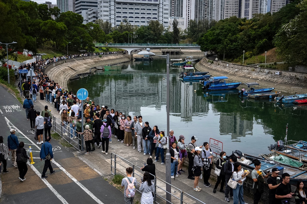 People line up to offer flowers and prayers for the victims near the site of a deadly Wednesday fire at Wang Fuk Court, a residential estate in the Tai Po district of Hong Kong's New Territories on Sunday, Nov. 30, 2025. (AP Photo/Chan Long Hei)